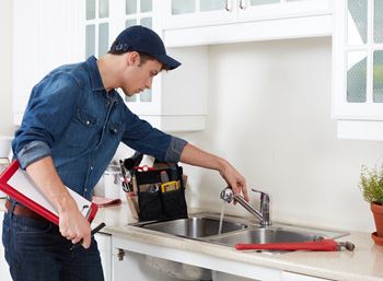Maintenance employee working on a repair on the kitchen sink.  He has a clipboard in hand and tool bag on the counter.